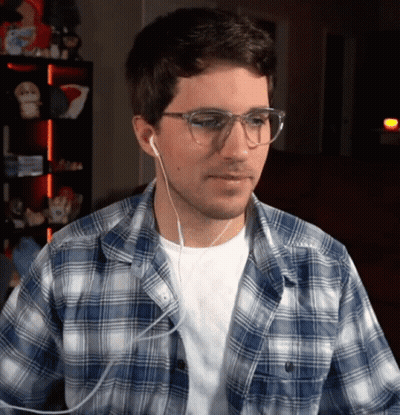 A Man Wearing A Plaid Shirt And Earbuds Looks At The Camera GIF