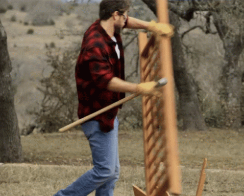 A Man Wearing A Plaid Shirt And Gloves Is Holding A Large Piece Of Wood GIF