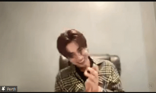 A Man Wearing A Plaid Shirt Is Sitting In A Chair And Smiling . GIF