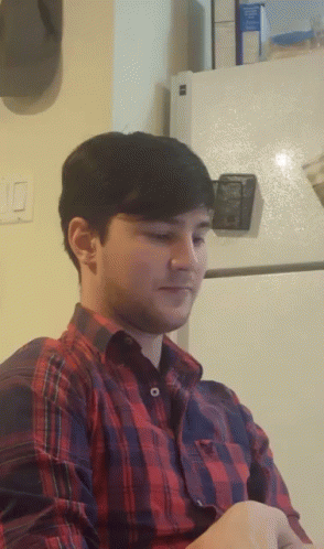 a man wearing a plaid shirt is sitting in front of a fridge