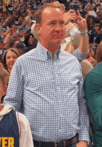 A Man Wearing A Plaid Shirt Is Standing In A Crowd Of People . GIF