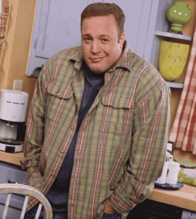 A Man Wearing A Plaid Shirt Is Standing In A Kitchen With His Hands In His Pockets GIF