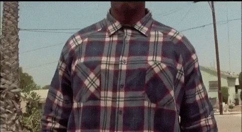 A Man Wearing A Plaid Shirt Is Standing In Front Of A Street . GIF