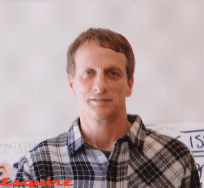 A Man Wearing A Plaid Shirt Is Standing In Front Of A Wall That Says Esquire On It GIF