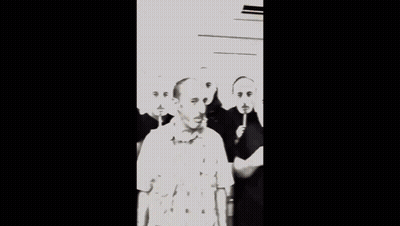A Man Wearing A Plaid Shirt Is Surrounded By Other Men With Red Faces On Sticks GIF