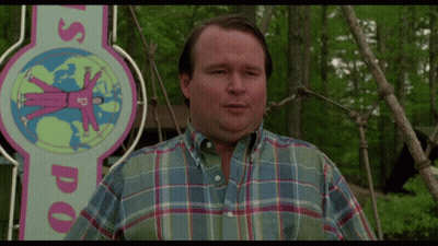 A Man Wearing A Plaid Shirt Stands In Front Of A Sign That Says Us Doo GIF
