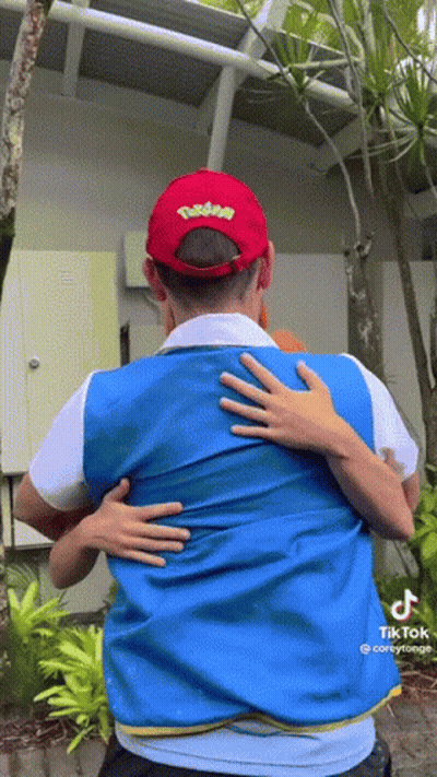 A Man Wearing A Pokemon Hat Is Hugging Another Man Wearing A Blue Vest GIF