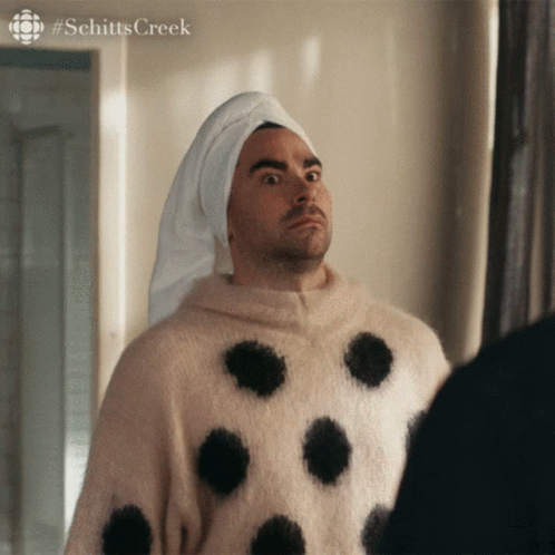 A Man Wearing A Polka Dot Sweater And A Towel Wrapped Around His Head Looks At Himself In The Mirror GIF
