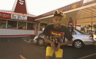A Man Wearing A Pulp Fiction T-Shirt Stands In Front Of A Mike 'S Restaurant GIF