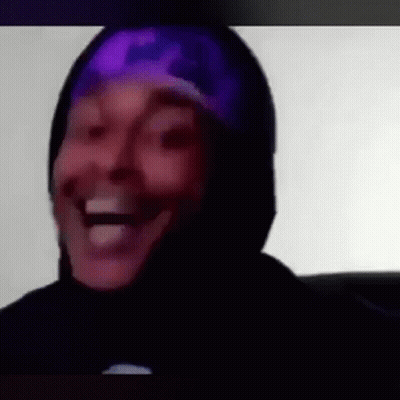 A Man Wearing A Purple Hat And A Black Hoodie Is Laughing . GIF