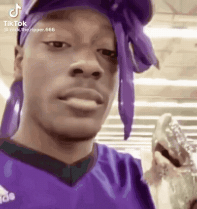 A Man Wearing A Purple Headband And A Purple Shirt Is Holding A Glass Of Water . GIF