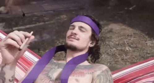 A Man Wearing A Purple Headband Is Smoking A Cigarette While Laying In A Hammock GIF