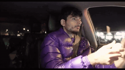 A Man Wearing A Purple Jacket Is Driving A Car GIF
