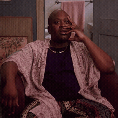A Man Wearing A Purple Shirt And A White Robe Sits In A Chair With His Hand On His Face GIF