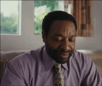 A Man Wearing A Purple Shirt And Tie Is Sitting On A Couch . GIF