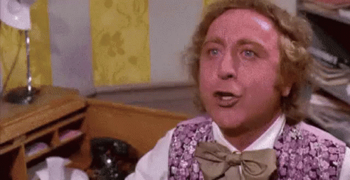 A Man Wearing A Purple Vest And Bow Tie Is Sitting At A Desk . GIF