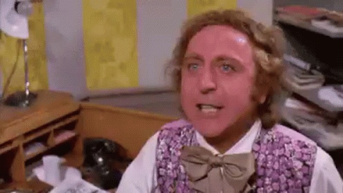 A Man Wearing A Purple Vest And Bow Tie Is Sitting At A Desk In An Office . GIF
