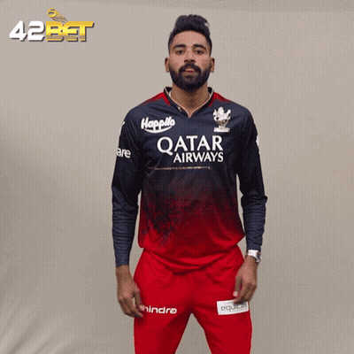 A Man Wearing A Qatar Airways Jersey Stands In Front Of A 42Bet Banner GIF