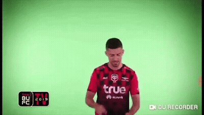 A Man Wearing A Red And Black Soccer Jersey Is Standing In Front Of A Green Screen . GIF