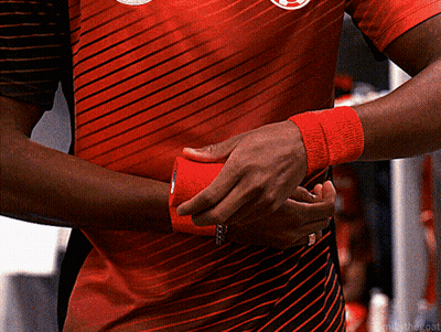 A Man Wearing A Red And Black Striped Shirt Is Wrapping His Wrist With Red Tape GIF