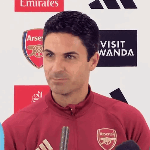 A Man Wearing A Red Arsenal Jacket Is Standing In Front Of A Sign That Says Visit Wanda . GIF