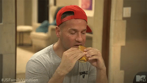A Man Wearing A Red Baseball Cap Is Eating A Hamburger . GIF