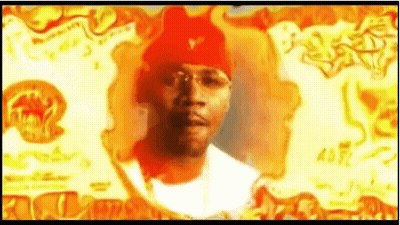 A Man Wearing A Red Beanie And Glasses Is Standing In Front Of A Fire . GIF