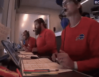 A Man Wearing A Red Buffalo Bills Sweater Is Sitting At A Desk GIF
