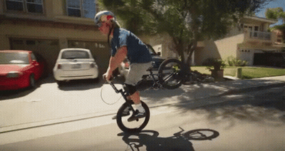A Man Wearing A Red Bull Helmet Is Riding A Bike On A Residential Street GIF