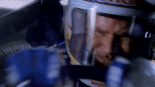 A Man Wearing A Red Bull Helmet Looks At A Can Of Soda GIF