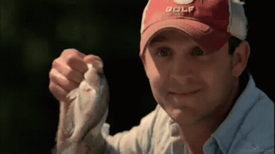 A Man Wearing A Red Golf Hat Is Holding A Small Fish In His Hand . GIF
