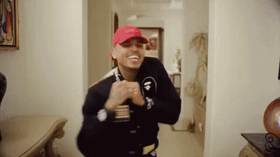 A Man Wearing A Red Hat And A Black Jacket Is Standing In A Hallway . GIF