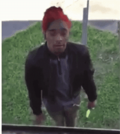 A Man Wearing A Red Hat And A Black Jacket Is Walking In The Grass . GIF