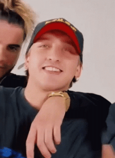 A Man Wearing A Red Hat And A Black Shirt Is Smiling . GIF