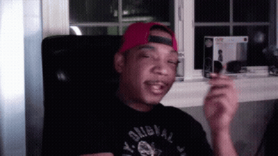 A Man Wearing A Red Hat And A Black Shirt That Says Y. Original Is Sitting In A Chair . GIF