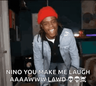 A Man Wearing A Red Hat And A Denim Jacket Is Laughing In A Dark Room . GIF