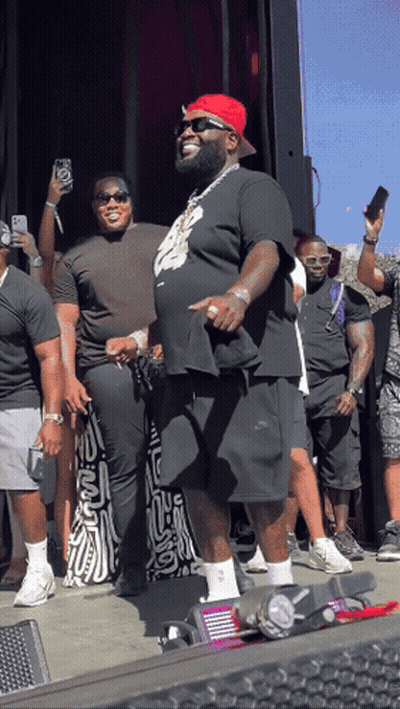 A Man Wearing A Red Hat And Sunglasses Stands In Front Of A Crowd Of People GIF
