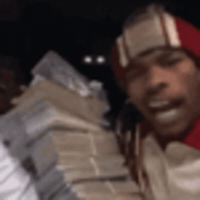 A Man Wearing A Red Hat Is Holding A Stack Of Money . GIF