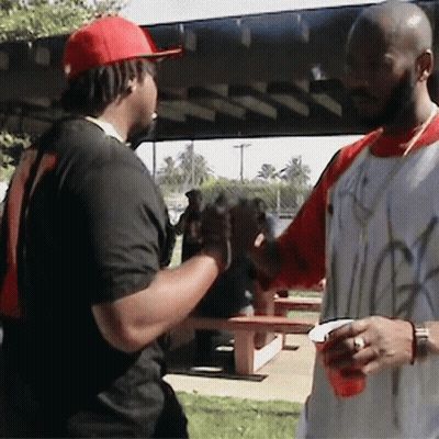 A Man Wearing A Red Hat Is Shaking Hands With Another Man Wearing A White Shirt With Graffiti On It GIF