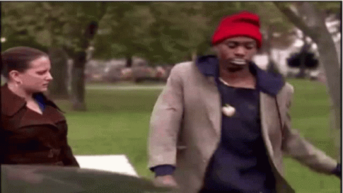A Man Wearing A Red Hat Is Walking In A Park With A Woman . GIF