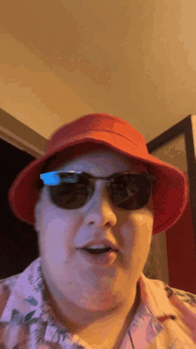 A Man Wearing A Red Hat , Sunglasses And A Pink Shirt Is Making A Funny Face . GIF