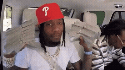 A Man Wearing A Red Hat With The Letter P On It Is Holding Stacks Of Money On His Shoulders . GIF