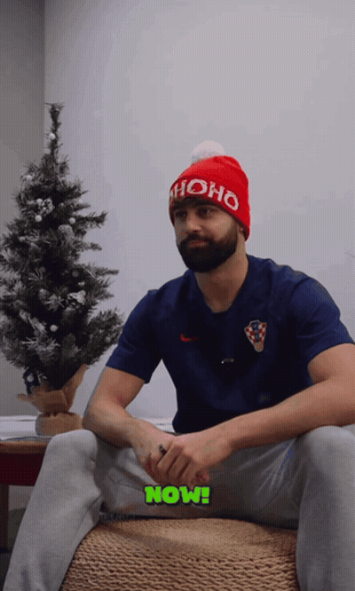 A Man Wearing A Red Ho Ho Hat Sits In Front Of A Small Christmas Tree GIF