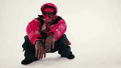 A Man Wearing A Red Jacket And A Bandana On His Face Is Squatting Down In The Snow . GIF