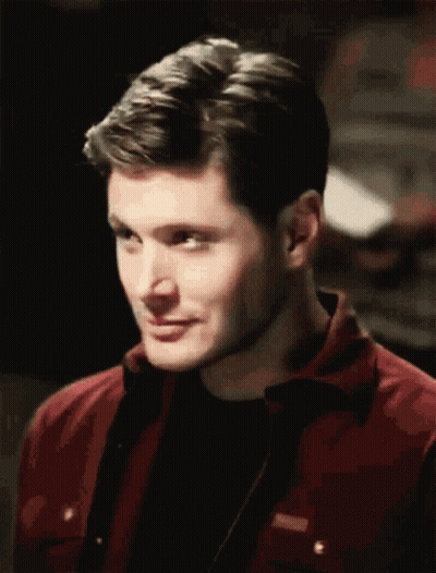 A Man Wearing A Red Jacket And A Black Shirt Is Smiling GIF