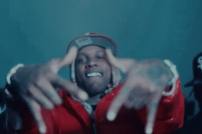 A Man Wearing A Red Jacket And A Hat Is Making A Hand Gesture . GIF