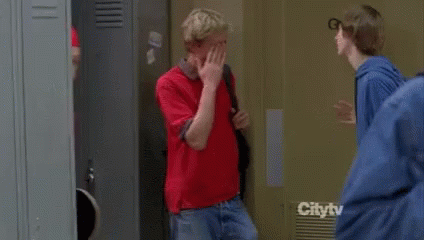 A Man Wearing A Red Jacket And A Music Band Shirt Is Carrying A Skateboard On His Shoulder . GIF