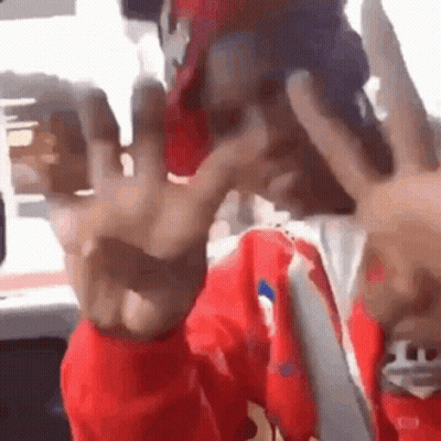 A Man Wearing A Red Jacket And A Red Hat Is Making A Peace Sign With His Hands . GIF