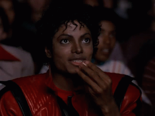 A Man Wearing A Red Jacket Is Eating Popcorn GIF