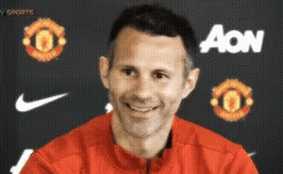 A Man Wearing A Red Jacket Is Smiling In Front Of An Aon Banner GIF